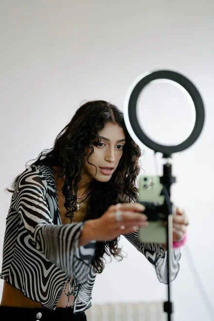 A woman setting a phone on a tripod under a ring light